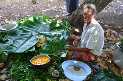 A Tongan woman is preparing food for the umu. To the left, notice the papaya and coconut milk dish.